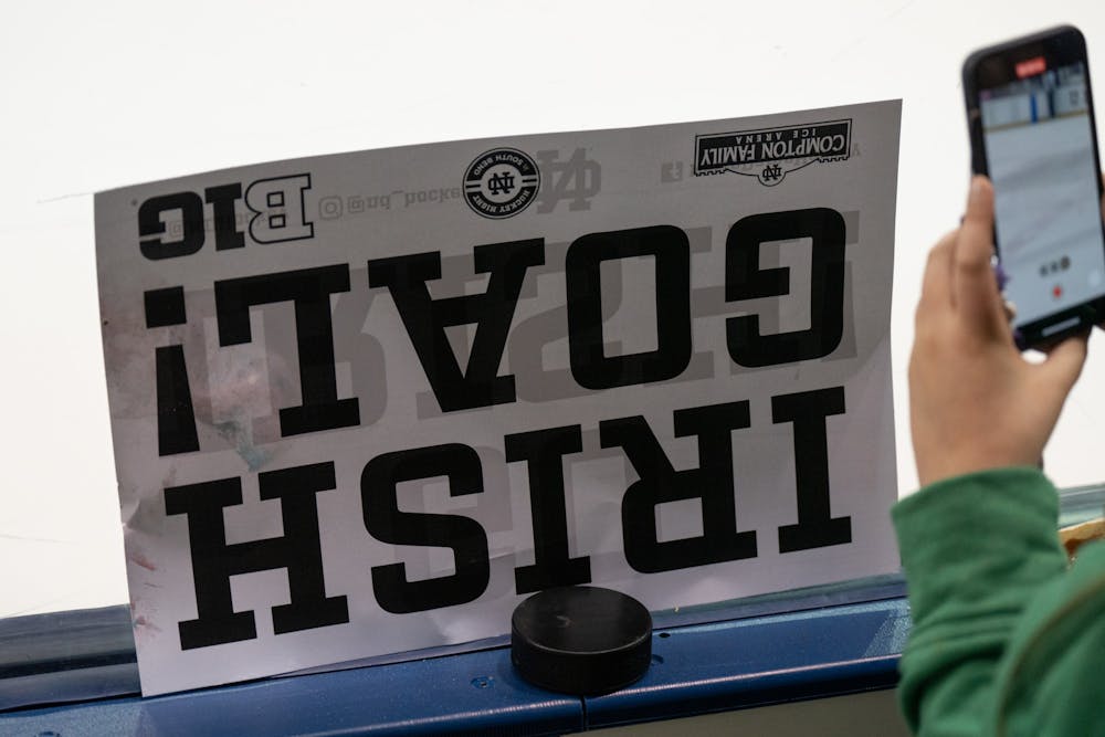 <p>A young fan’s lucky catch rests on the boards while she uses her phone to record the game at Compton Family Ice Arena in Notre Dame, IN on Friday, March 4, 2023. Over 5,000 fans attended the game in a sellout game.</p>