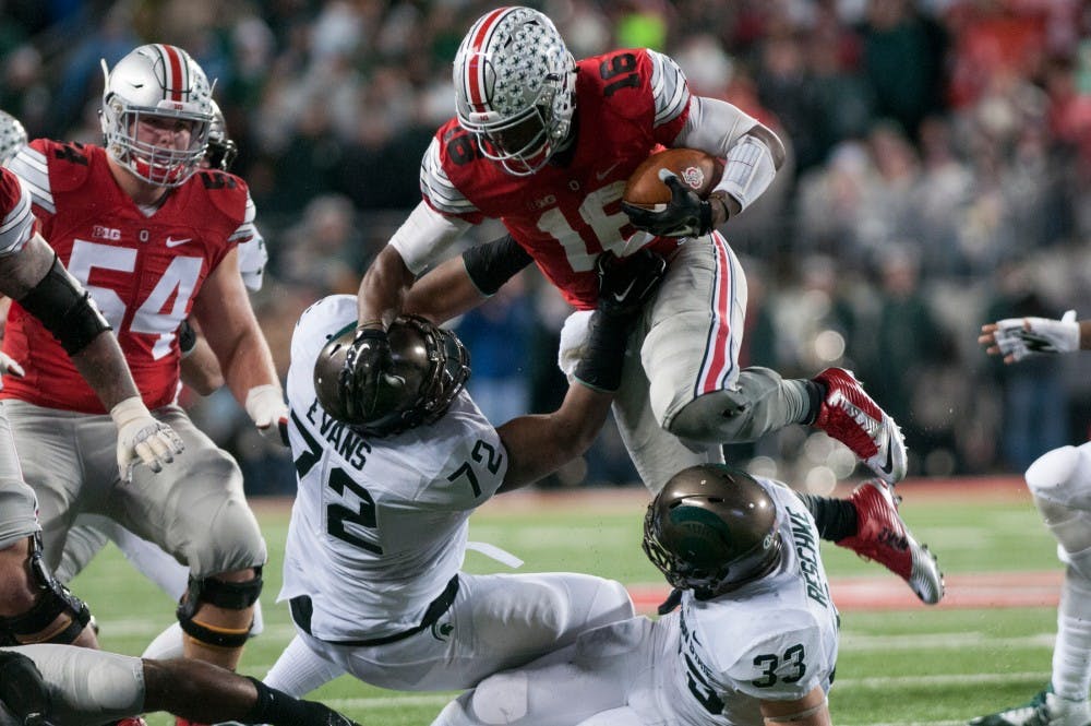 <p>Red-shirt freshman defensive tackle Craig Evans, 72, and sophomore linebacker Jon Reschke, 33, tackle Ohio State quarterback J.T. Barrett during the third quarter of the football game against Ohio State on Nov. 21, 2015 at Ohio Stadium in Columbus, Ohio. The Spartans defeated the Buckeyes, 17-14.</p>