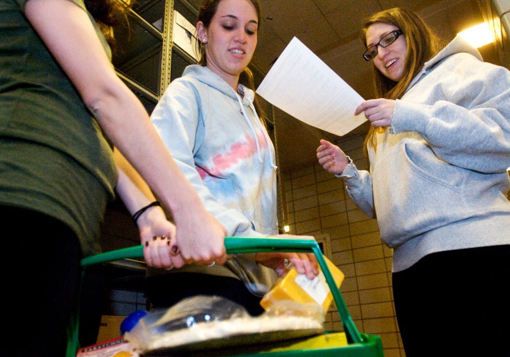 Speech pathology sophomore Sarah Silver holds a basket of food as social work sophomore Alana Kingsley adds another item and Evie Chutz, also a social work sophomore, consults a list of items Wednesday at the MSU Food Bank within Olin Health Center. All three were volunteering through the Hillel Jewish Student Center, which organized a group of students to assist at the food bank. Kat Petersen/The State News