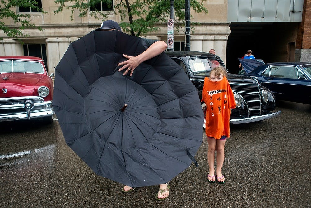 	<p>Mason, Mich., resident Rob Palmer tries to collapse his umbrella, while his daughter Georgia Palmer, 7, stands in the rain, July 27, 2013, in downtown Lansing during the Car Capital Auto Show 2013. The 21st annual event was organized by the R.E. Olds Transportation Museum. Justin Wan/The State News</p>
