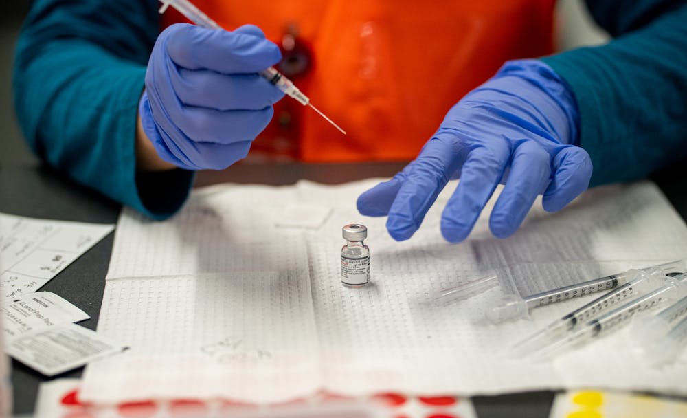 <p>Kamaya Young fills vaccine syringes, sorting them by vaccine, during the COVID-19 vaccine booster clinic at the Breslin Center on Jan. 26, 2022. The vaccine she works with here is Pfizer, but she was filling both Moderna and J&amp;J as well.</p>