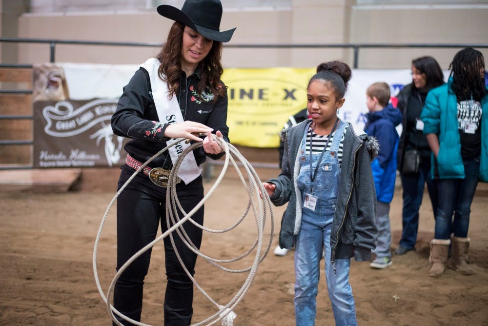 Sophomore agribusiness Claire Daugherty, left, explains how to lasso a cow as Jaleia Taylor, age 9, listens during the Spartan Stampede kid's day on Feb. 19, 2016 at the MSU Pavilion for Agriculture and Livestock Education.