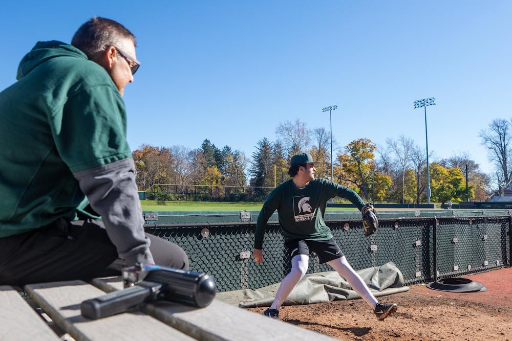 Michigan State sophomore right-handed pitcher Gavin Moczydlowsky (22) practices in the bullpen at McLane Stadium on Nov. 7, 2024. MSU assistant and pitching coach Mark Van Ameyde sits next to the radar gun that is used for tracking the speeds of the players pitches. 