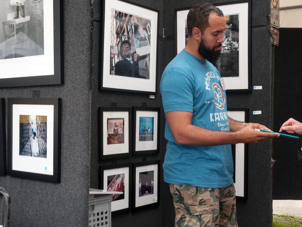 <p>Clifton Henri makes a sale with a customer May 17, 2015 at the East Lansing Art Festival. Henri has sold art at the festival several times but this is his first year back after taking a couple years off to tend to his studio space in his hometown of Chicago. Asha Johnson/The State News</p>