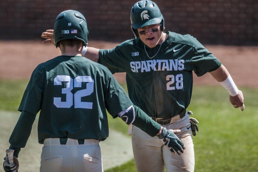 Freshman catcher Adam Proctor (28) high fives freshman second baseman Zach Iverson (32) after scoring on a passed ball during the game against Nebraska on April 8, 2018. The Spartans defeated the Cornhuskers, 5-3. (C.J. Weiss | The State News)