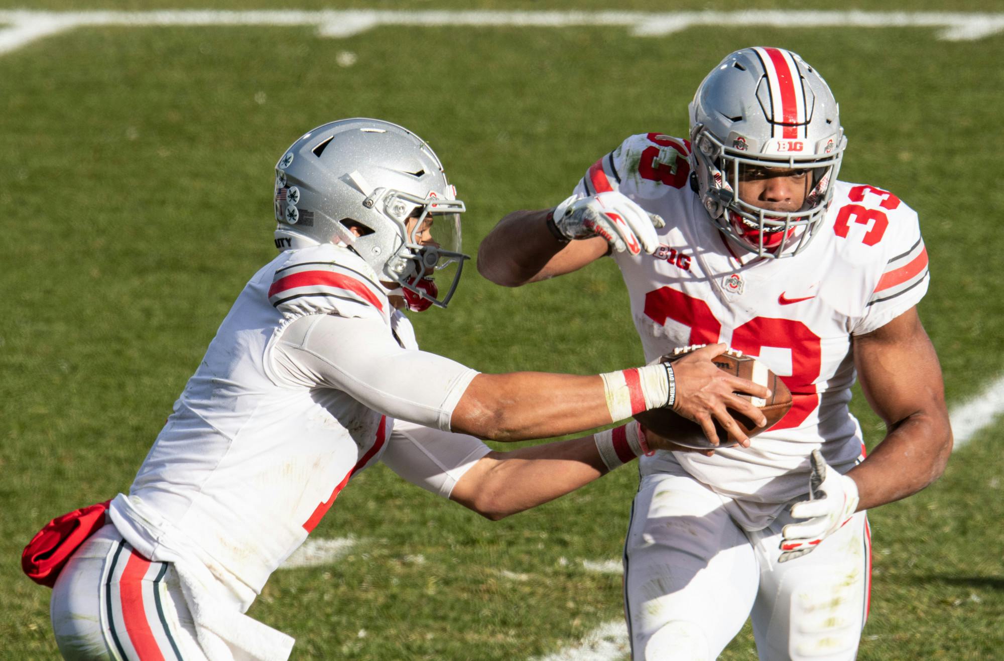 <p>OSU quarterback Justin Fields (1) hands the ball off to Chris Booker (33) in a game against MSU on Dec. 5, 2020.</p>