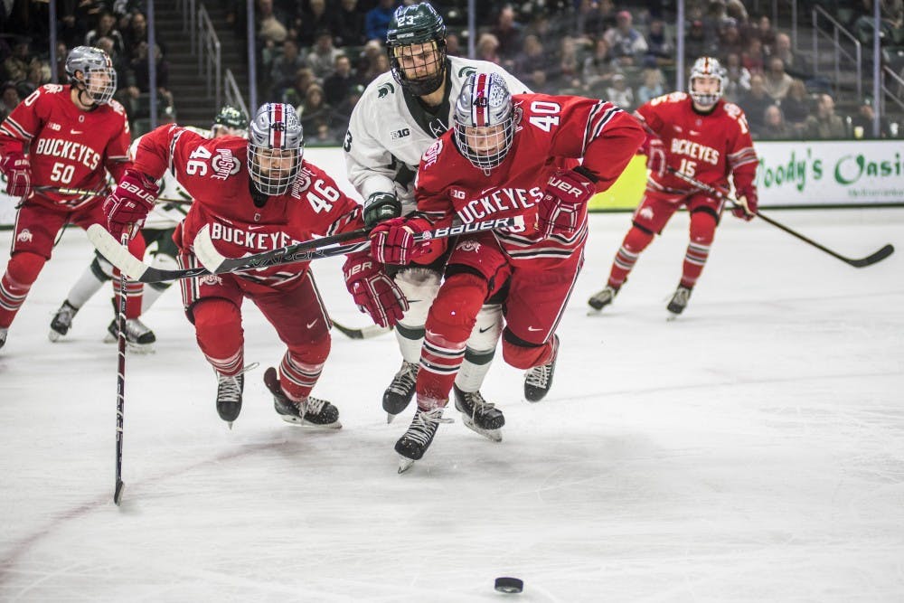 Junior center Cody Milan (23) and Ohio State's Matt Joyaux (46) and Ronnie Hein (40) go after a loose puck during the men's hockey game against Ohio State on Jan. 5, 2018 at the Munn Ice Arena. The Spartans were defeated by the Buckeyes, 4-1. (Nic Antaya | The State News)
