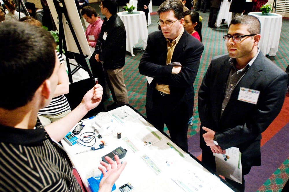 Investors from the Michigan Accelerator Fund Prem Bodagala, right, and Dale Grogan listen to Mike Anderson describe the Nano-BEAMs and Biosensors: Method and Device to Rapidly Detect Infectious Diseases project he helped to develop Tuesday evening at the Spartan Innovation Celebration. The event, held in the Union Ballroom, was put on by MSU Technologies to showcase scholarship and discovery at the university. Matt Hallowell/The State News