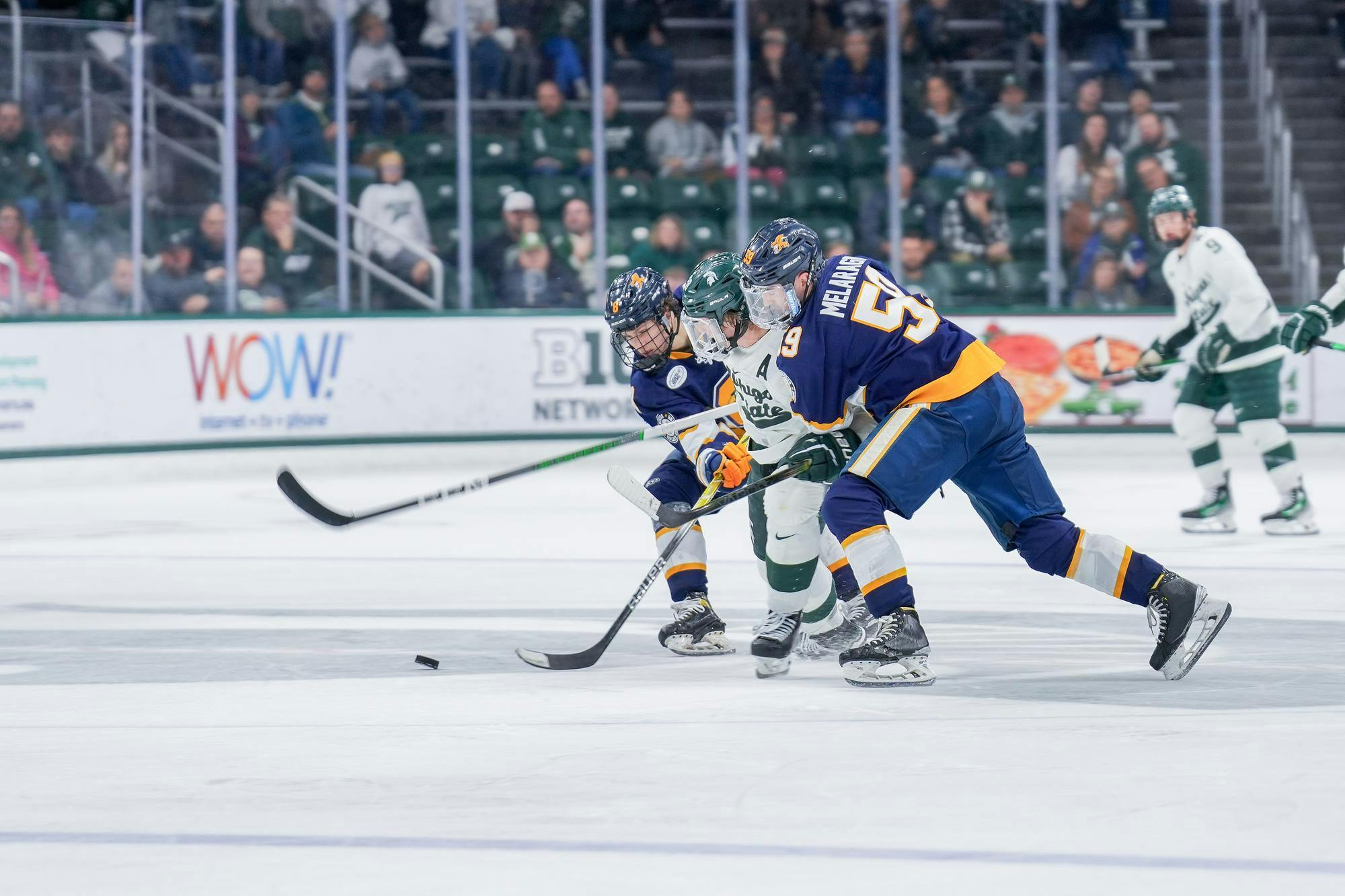 <p>Two Canisius players on either side of a Michigan State player during a game between each other at Munn Ice Arena on Oct. 19, 2023. The Spartans beat the Griffins 6-3 in one of a two-game series.</p>