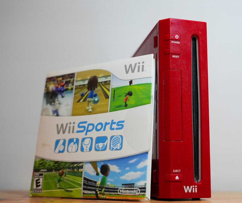 A copy of Wii Sports sits next to a red Nintendo Wii console on a table.