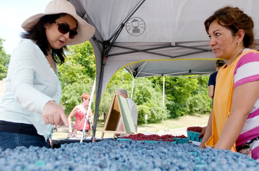 	<p>Hiroko Nagahata, left, a music graduate student, points to a quart of blueberries to purchase from Elvira Garza, who grows the berries with her husband, Sunday at the opening day of the East Lansing Farmer&#8217;s Market at Valley Court Park, 201 Hillside Court.</p>