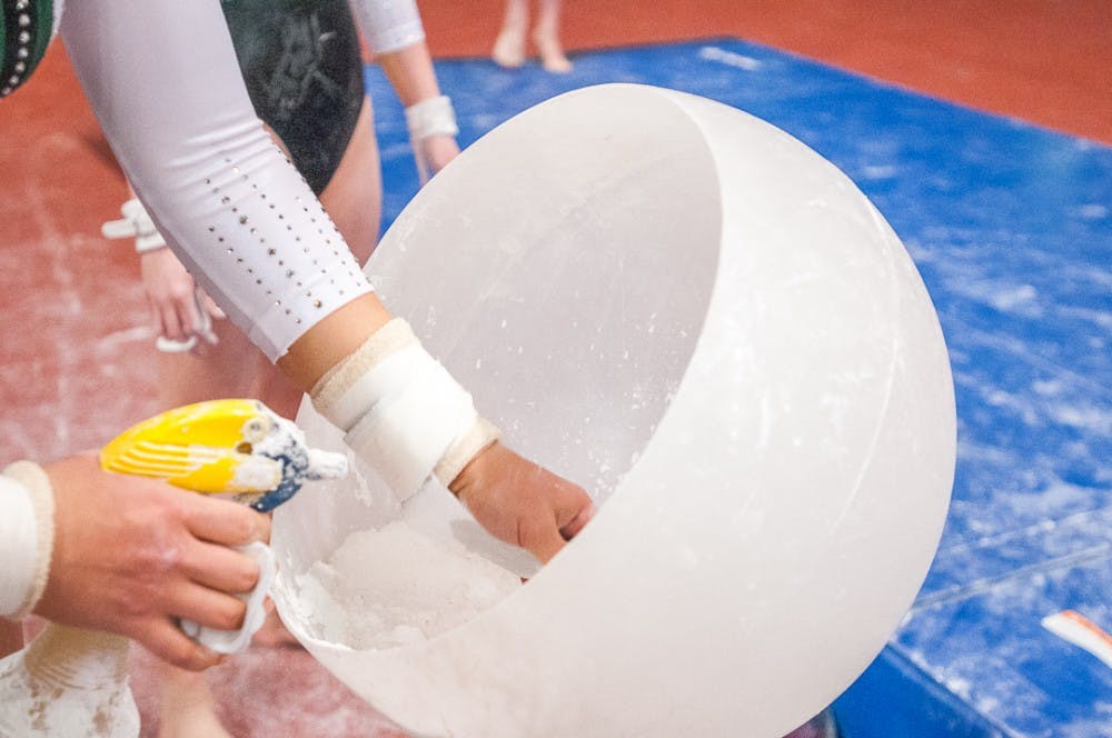 <p>A gymnast chalks up their hands before performing on the uneven bars during the event against Illinois on Feb. 17, 2018 at Jenison Fieldhouse.&nbsp;</p>