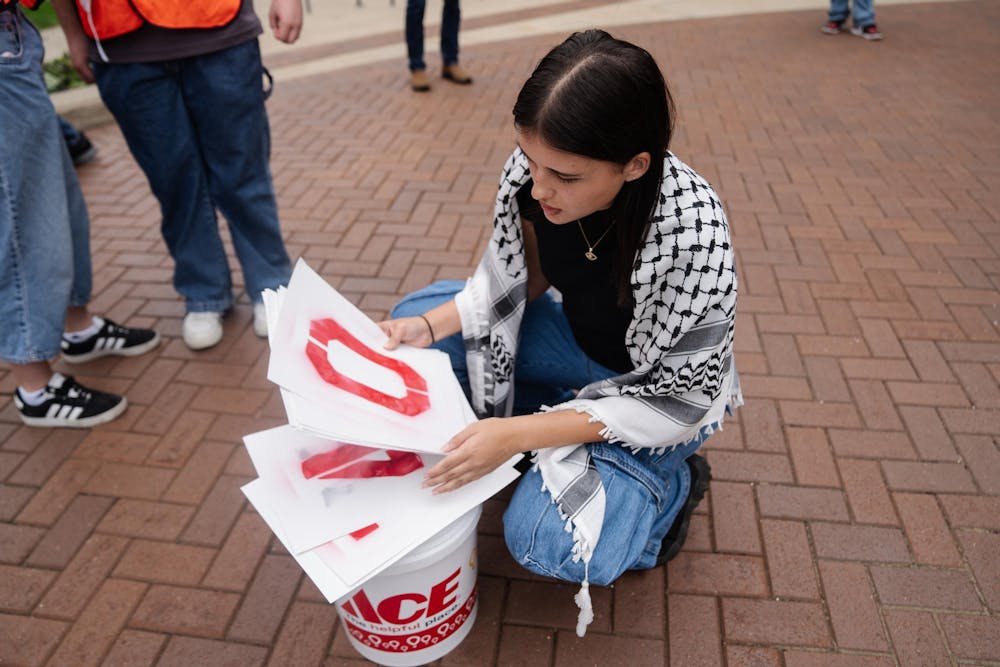 <p>Students for Justice in Palestine member Jaime Saliba organizes “Divest Now!” signs outside of the Wharton Center on Sept. 29. 2024. The signs were numbered 1-10 for protestors to line up in order according to number.</p>
