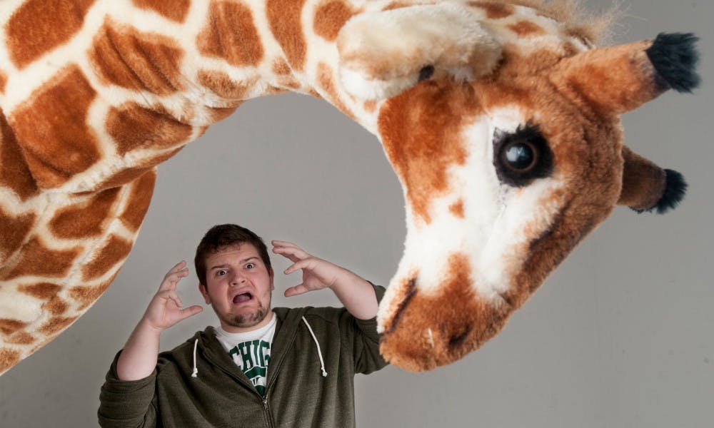 <p>Media and information freshman Alec Comes poses for a portrait with "Schneebly" the Giraffe House Comedy Club mascot on Oct. 22, 2015 at the State News. Comes carries "Schneebly" around to advertise the club. </p>