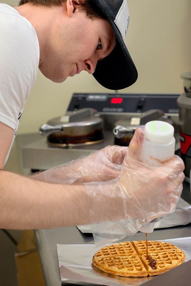 	<p>Matt Wilbur, employee of Wandering Waffles, adds ingredient to a waffle, July 24, 2013, at the store&#8217;s location at Lansing City Market, 325 City Market Drive, in Lansing. The bakery has been operating since this March. Justin Wan/The State News</p>