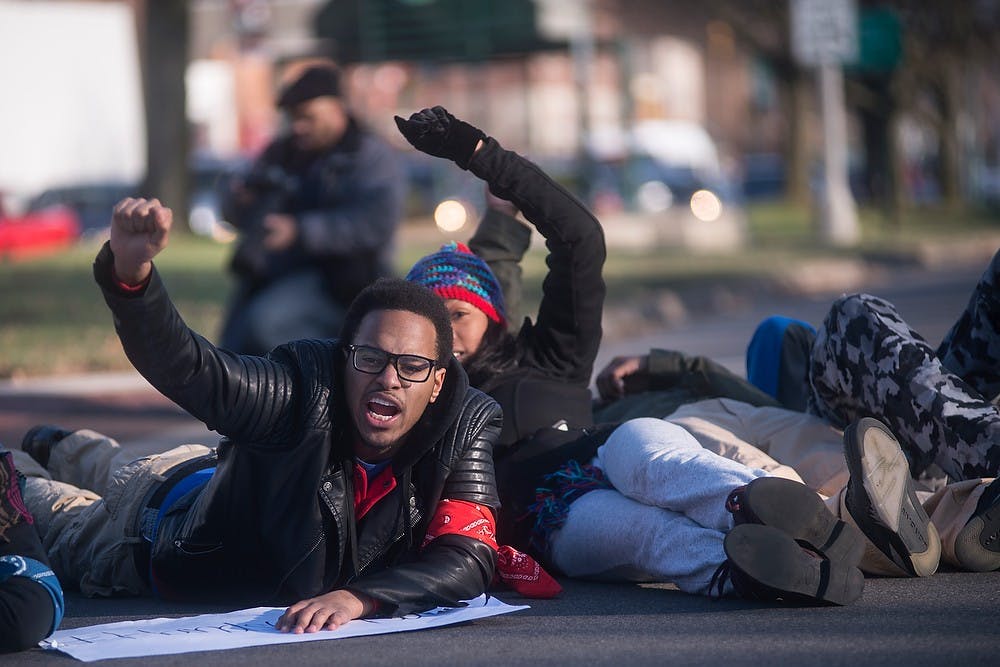 <p>Supply chain management sophomore Steve Cleaves-Jones chants and lays down in the middle of Grand River Ave. in protest Dec. 6, 2014, during a protest which went down Grand River Ave., to the MSU Union and ended to the Beaumont Tower. The group of students shut down Grand River Ave., in East Lansing by marching and laying down in the middle of the street in protest of police violence against black people. Erin Hampton/The State News</p>