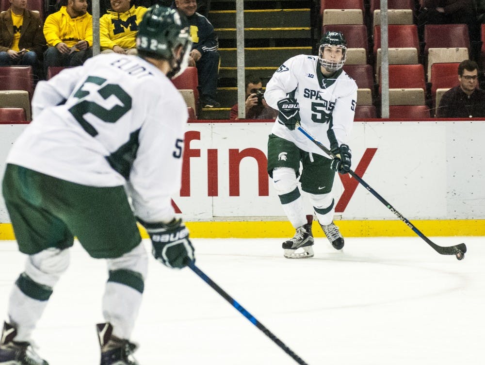Redshirt freshman Jerad Rosburg (57) passes the puck to freshman defenseman Mitch Eliot (52) during the first period of the 52nd Annual Great Lakes Invitational third-place game against the University of Michigan on Dec. 30, 2016 at Joe Louis Arena in Detroit. The Spartans were defeated by the Wolverines in overtime, 5-4.