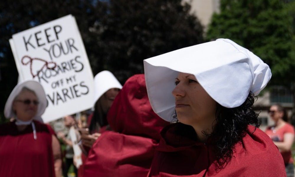 <p>Protest attendees wear red robes and white hats at Michigan State Capitol on June 22.</p><p></p>