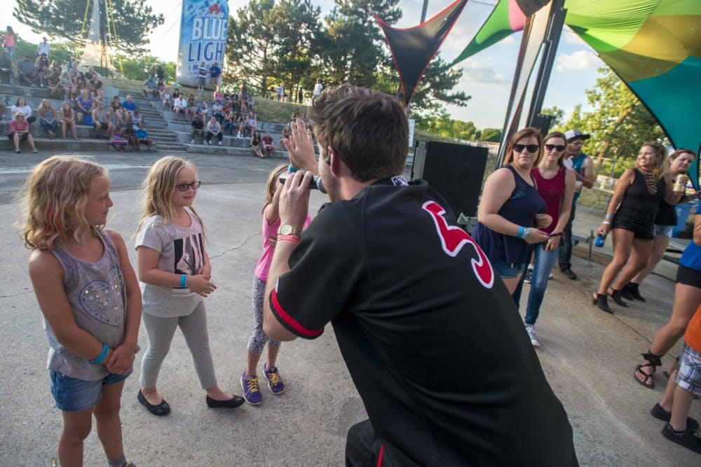 From left to right, East Lansing residents Luci Hylen and Allison Drzal watch Annika Drzal high five Kid Quill during Common Ground Music Festival on July 10, 2016 at Adado Riverfront Park in Lansing.