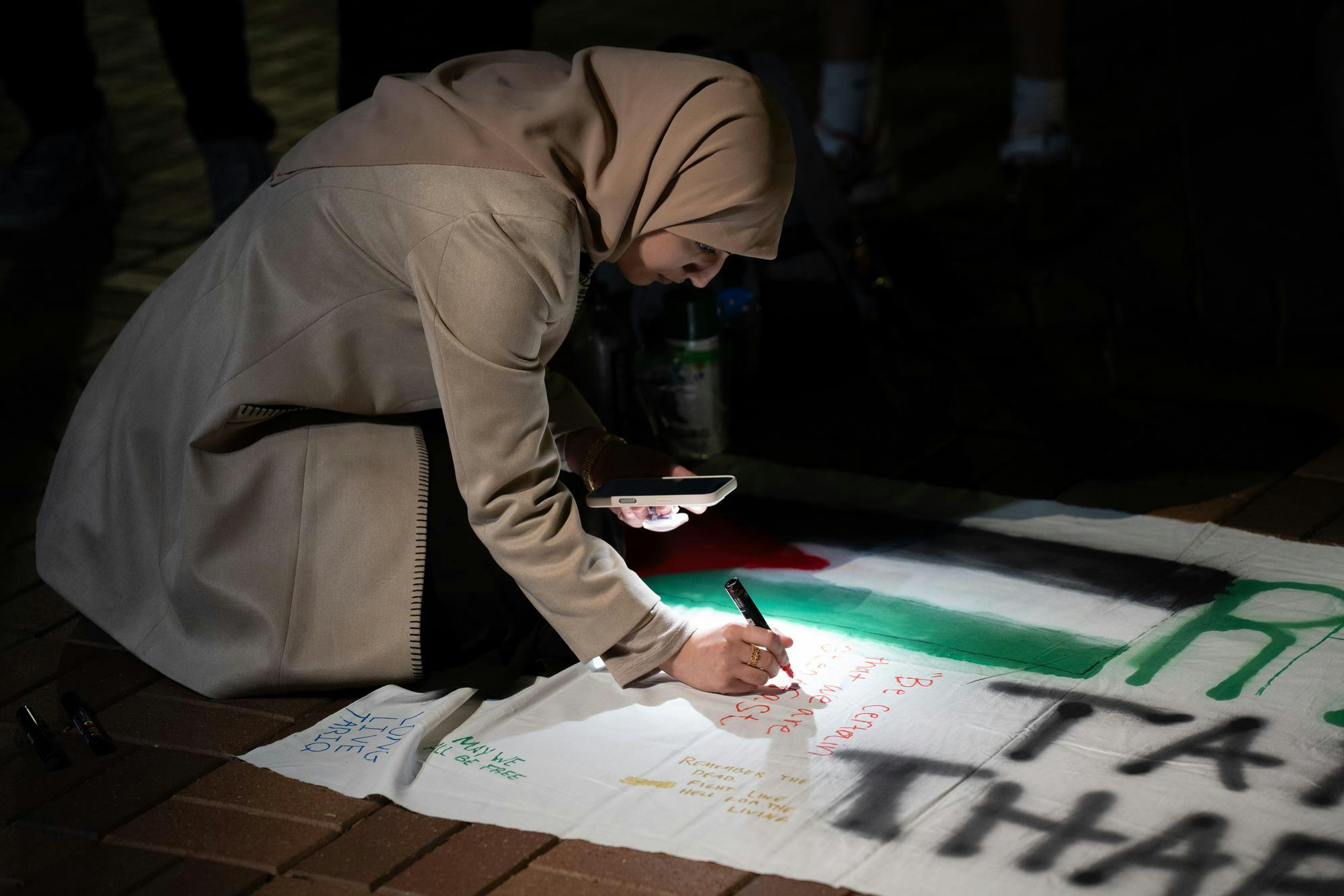 <p>Human biology junior Aesha Zakaria writes "Be certain we are steadfast" onto a banner at an anniversary memorial for Michigan State Humphrey fellow and Israeli bombing victim Tariq Thabet on Oct. 30, 2024.</p>