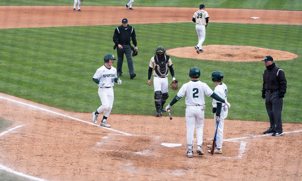 MSU catcher Noah Bright, tongue hanging out, meets his teammates' embrace at home plate at McLane Baseball Stadium in East Lansing on Wednesday, March 27, 2024. Bright slammed a home run over the left field fence to cut Oakland's lead to 3.