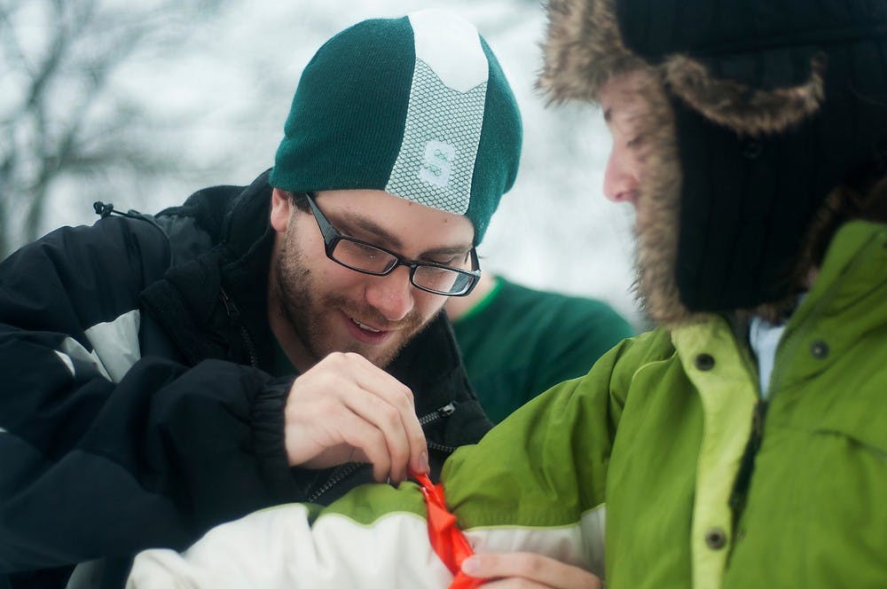 	<p>Novi, Mich. resident and alumnus Scott Kelber ties a strip onto second year veterinary student Lauren Fischer on Jan. 11, 2014, behind the rock on Farm Lane. The group of friends gathered to play a game of football in the snow before heading to the Dairy Store. Danyelle Morrow/The State News</p>