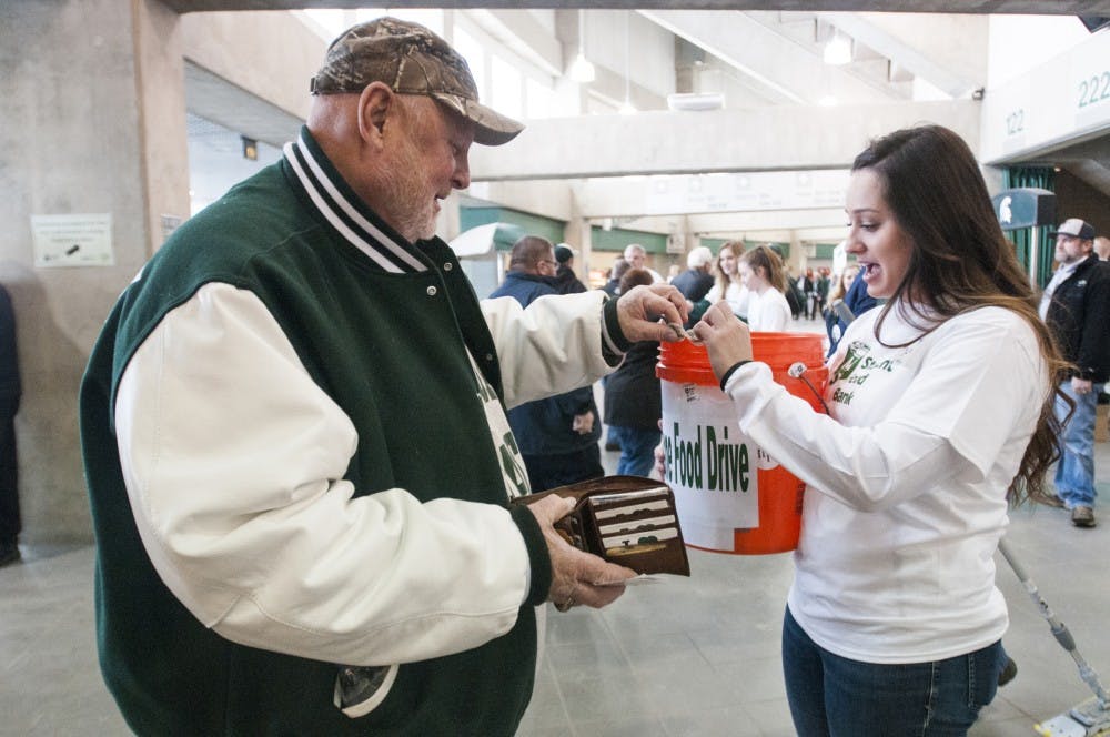 Dimondale resident Steve Markucki hands his donation to supply chain management junior Madison Walker during the MSU Rebounders Club Annual Food Drive on Jan. 29, 2017 at Breslin Center. Lupe Izzo has planned this event in coordination with the MSU Student Food Bank for 23 years. The proceeds and food raised from the fundraiser will be split evenly between the MSU Student Food Bank and Greater Lansing Food Bank. 