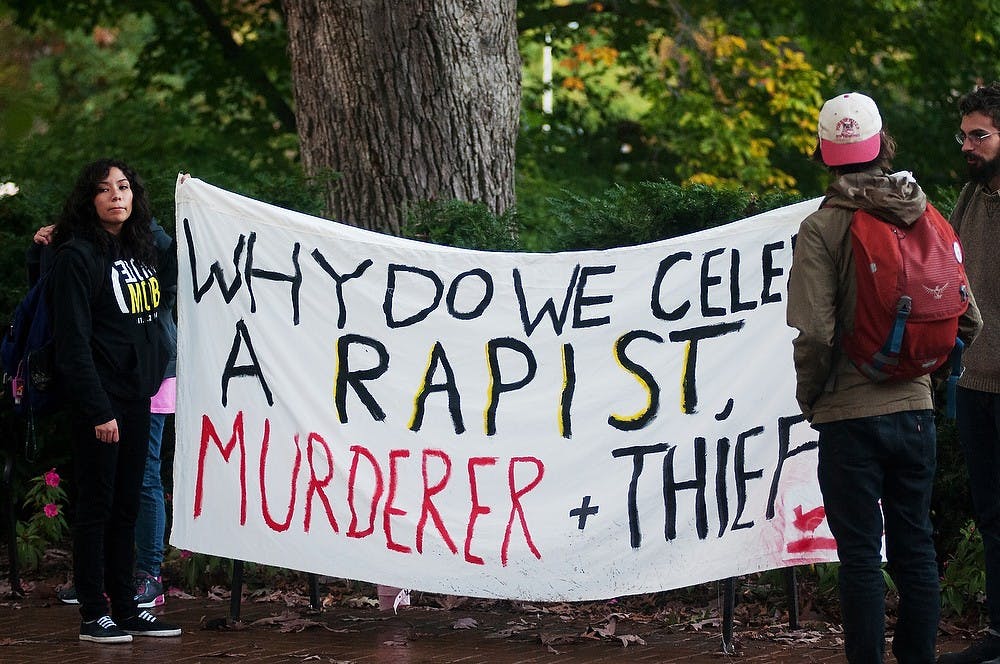 <p>Comparative culture and politics sophomore Lizbeth Lopez, left, holds a banner as philosophy senior Spencer Perrenoud, right, wait for the protest to begin Oct. 13, 2014, at the Beaumont Tower. The North American Indigenous Students Organization protested from the Beaumont Tower to The Rock on Farm Lane. Aerika Williams/The State News</p>