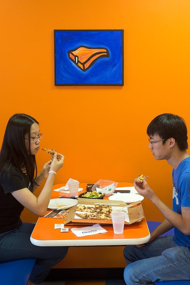 <p>Graduate students Stella Qian and Jingtai Liu eat a Hawaiian pizza Sept. 9, 2014, at Cottage Inn Pizza, 615 East Grand River Ave. Qian, who has been to Cottage Inn twice, said she enjoys the pizzas they offer. Julia Nagy/The State News</p>