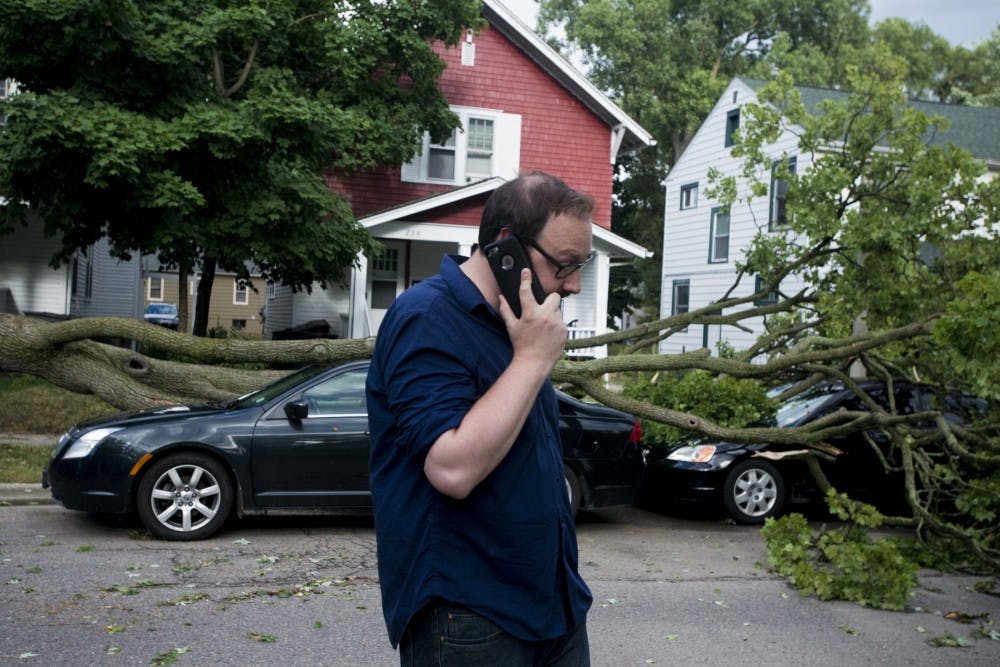 Communications manager of MSU residential hospitality Casey Bye talks on the phone as he waits for assistance to remove the fallen tree from his car on July 8, 2016 on Bailey St. Bye was in his parked car when the tree fell.
