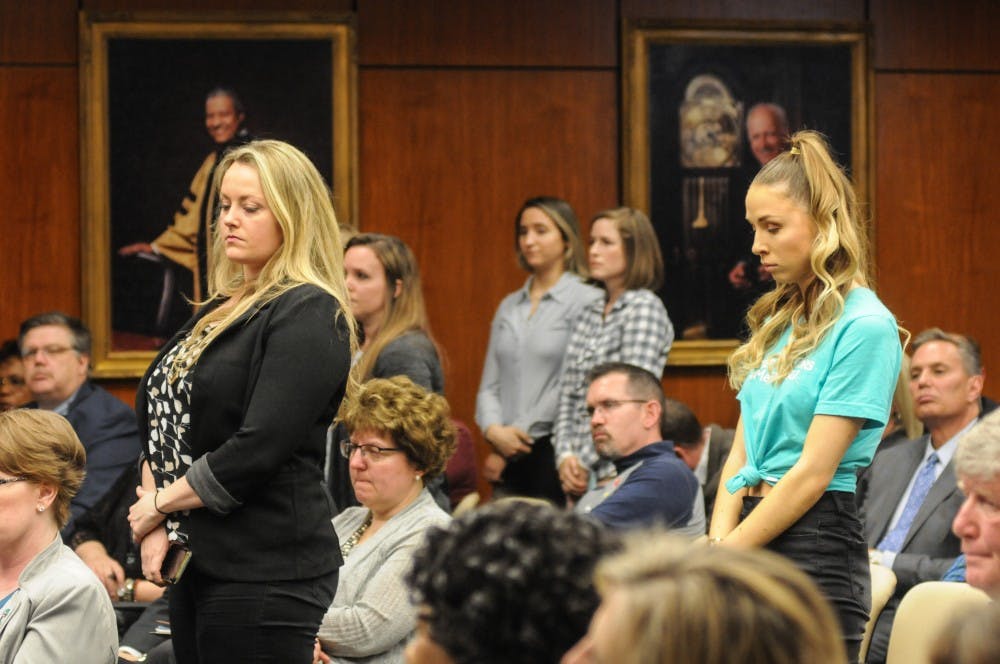 <p>Survivors stand in the audience at the Board of Trustees meeting on April 12, 2019 at the Administration Building.</p>