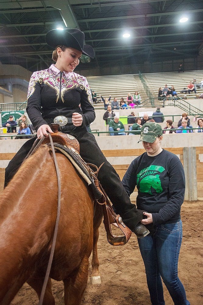 <p>Senior Katherine Walker receives help from a team member to pull up her chaps Jan 18, 2015, during MSU's Horsemen Weekend at The MSU Pavilion, 4301 Farm Ln. in East Lansing. Walker has been in every show since her freshman year and placed first in her show, giving her two first place ribbons. Emily Nagle/The State News</p>