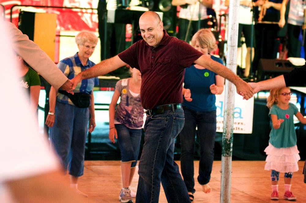 <p>East Lansing resident John Kodeski holds hands and spins in a circle with other men participating in a group polka Sunday at the Great Lakes Folk Festival in East Lansing. </p>