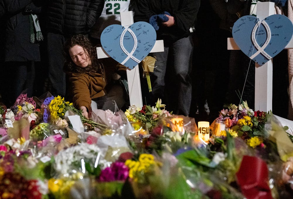 <p>An MSU student lays a bouquet of flowers on the ground in front of the Rock on Farm Lane during a vigil event on campus on the evening of Feb. 15, 2023.</p>
