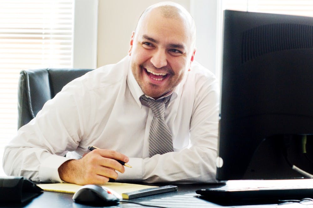 Owner of Full Circle Financial Planning, Jose Yanez is all smiles Wednesday afternoon as he sits at his desk. Yanez's business provides financial advice and counseling to their customers, and they hope to expand their clientele to the MSU students and employees. Anthony Thibodeau/The State News