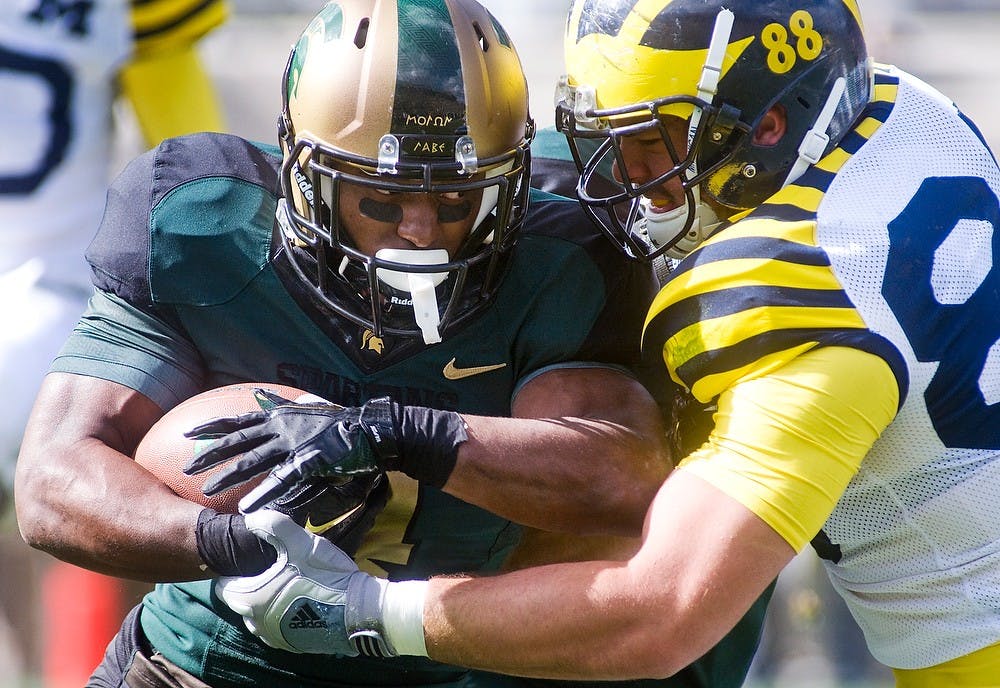 <p>Junior running back Edwin Baker hangs onto the ball as Michigan defensive end Craig Roh wraps him up Oct. 15, 2011, at Spartan Stadium. The Spartans defeated the Wolverines 28-14. State News File Photo</p>