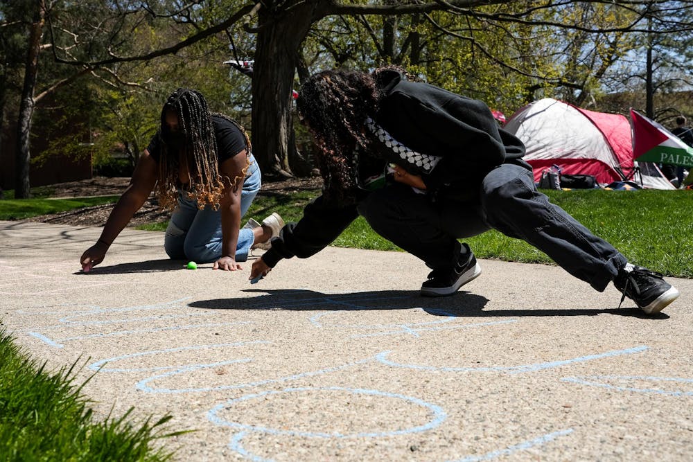 Michigan State University students write on the sidewalk with chalk near the Gaza solidarity encampment in People’s Park on MSU’s campus on April 25, 2024.