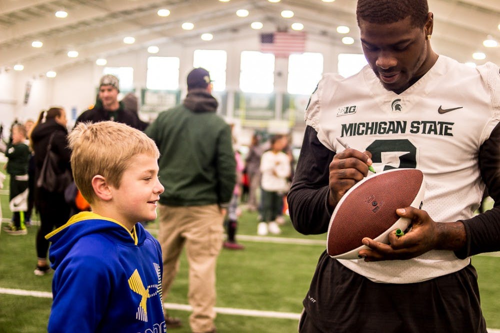 <p>Grand Ledge resident Ashton Delaney, 9, watches senior running back LJ Scott (3) sign his football during the youth clinic on April 7, 2018 at Duffy Daugherty Football Building.</p>