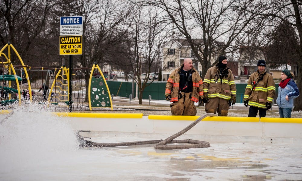 East Lansing firefighter Joe Pontack, left, East Lansing firefighter Dan Renner, center left, East Lansing firefighter Nate Floyd, center right, and community development analyst for the city of East Lansing?s planning, building and development Amy Schlusler, right, watch as the skating rink fills on Jan. 27, 2017 at Valley Court Park at 300 Valley Ct. in East Lansing. This is the second year that East Lansing has offered an outdoor iceskating rink.