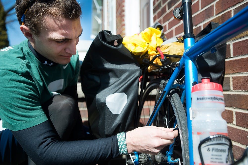 <p>Advertising senior Derek Blalock checks his tire pressure April, 1, 2015, in front of his house on Gunson Street in East Lansing. Blalock plans to make the 260 mile trip to Indiana this weekend on his bike. He said his friend will give him a ride back to campus. Erin Hampton/The State News</p>