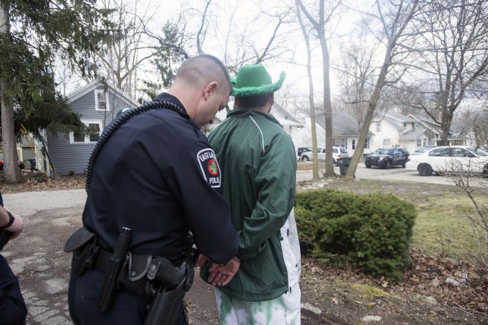 Officer Ryan Kuhn arrests a man after urinating on the side of a house on March 17, 2016 on Marshall St. in East Lansing. 