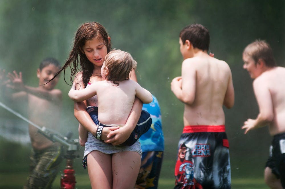 Dawn Garcia, 13, from Lansing, spins with her younger brother Ramon Garcia, 1, while playing in the sprinkler Monday, May 28th, 2012 at Lake Lansing. The two were spending their day at the lake with family for Memorial Day. Samantha Radecki/The State News