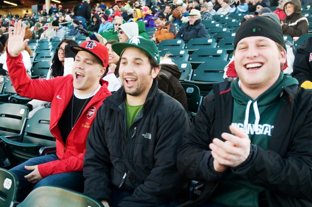 From left, finance senior Jarrett Nelson, economics senior Michael Emmer and hospitality business senior Ian Gross wave to Sparty as he makes his way around Cooley Law School Stadium on Tuesday for the Crosstown Showdown between the MSU baseball team and the Lansing Lugnuts. All three seniors said attending the game was on their senior bucket list. Kat Petersen/The State News