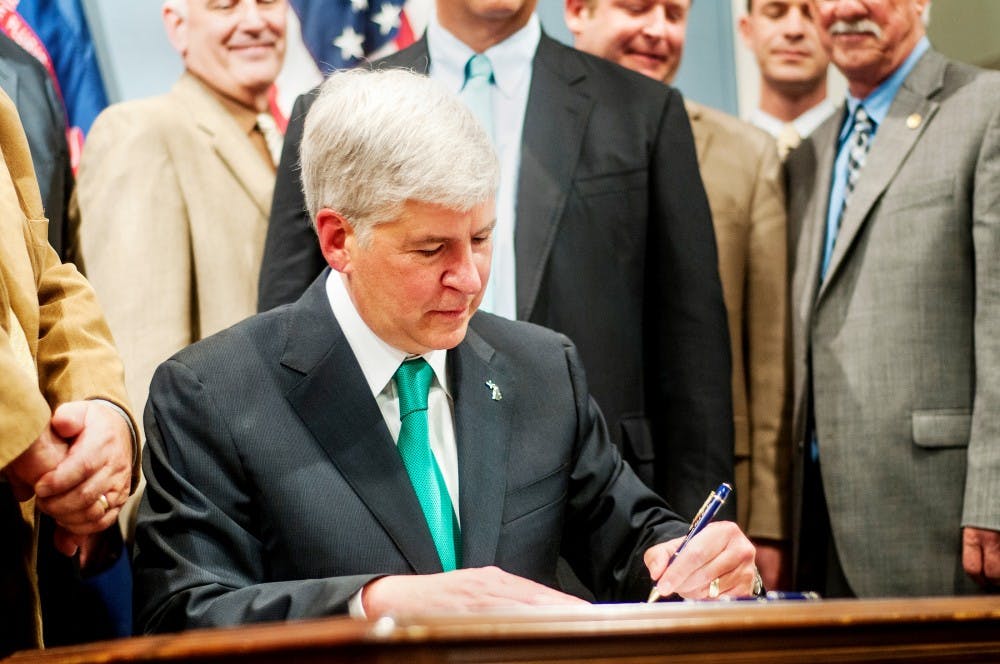 Governor Rick Snyder signs the 2012-2013 fiscal year budget as legislatures stand by Tuesday June 26, 2012 at the George W. Romney building in Lansing.  MSU is receiving just under $3 million from the higher education portion of the budget with the overall state budget totaling $48 billion. Adam Toolin/The State News