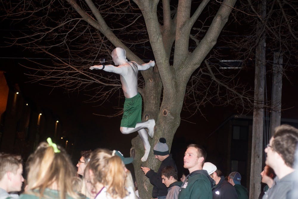 A student climbs a tree to gather GoPro footage of the crowd on Dec. 5, 2015 in Cedar Village. Hundreds of students gathered in the streets of Cedar Village to celebrate MSU's victory over Iowa in the Big Ten championship, resulting in police action.