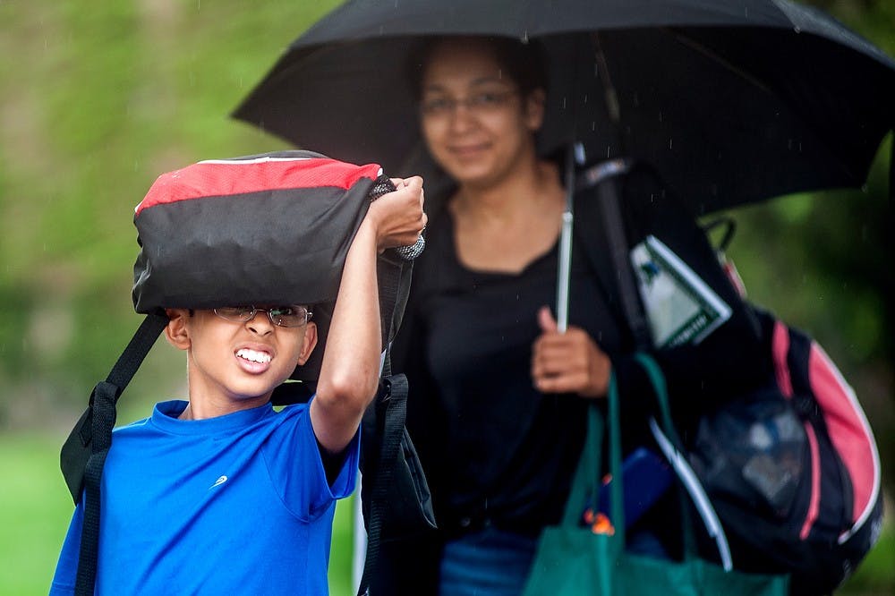 	<p>Parin Patel, 14, holds his backpack over his head to shield himself from the falling rain as he walks with Arden McFarlane, both from Raleigh, N.C., May 22, 2013, on North Shaw Lane. Patel is a participant of the 2013 Odyssey of the Mind World Finals that are currently underway on campus from May 22-25, while McFarlane is a parent who traveled with the team. Weather in East Lansing saw a high of 75 degrees Wednesday afternoon with rain showers and thunderstorms likely to continue until Thursday night. Justin Wan/The State News</p>