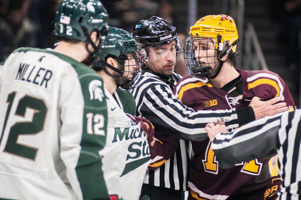 A referee puts his arms between players during the game against Minnesota on Jan. 18, 2018 at Munn Ice Arena. The Spartans fell to the Gophers 5-4.