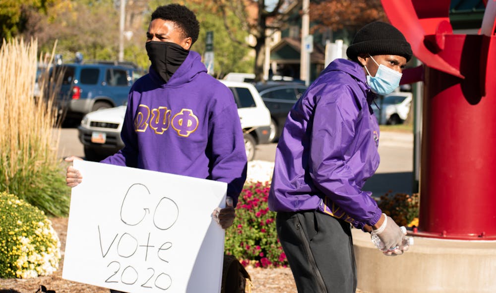 <p>Anthony Hines Jr. (left) and Ryan Thomas (right) of MSU&#x27;s Omega Psi Phi station outside of the East Lansing clerk&#x27;s office Nov. 3, 2020, motivating people to vote on Election Day by giving out free water. </p>