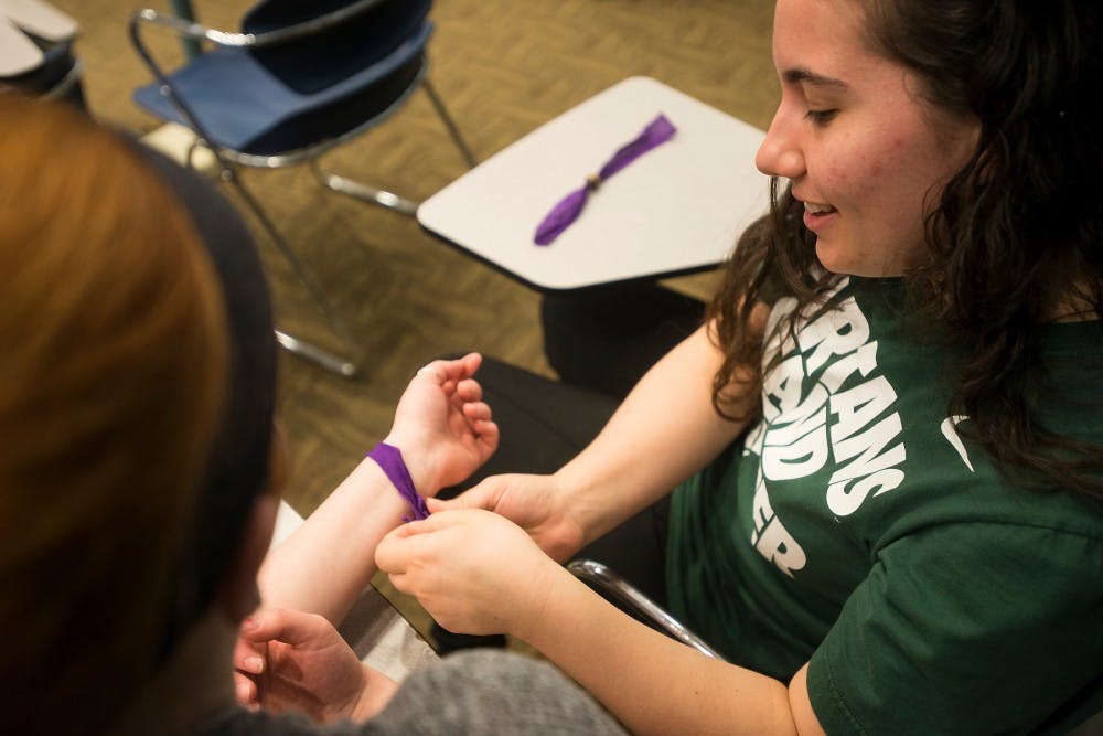 <p>Biochemistry and Molecular Biology junior Char Panek, left, ties a bracelet onto psychology senior Nicole Thompson's wrist April 1, 2015, during Embrace the Rain at Erkison Kiva on Farm Lane. Embrace the Rain wa san event to spread the awareness of mental health issues and gave people a forum to give their own testimony. Erin Hampton/The State News</p>