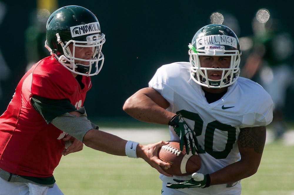 	<p>Senior quarterback Andrew Maxwell hands off the ball to junior running back Nick Hill during practice Aug. 14, 2013, at the practice field outside Duffy Daugherty Football Building. Julia Nagy/The State News</p>